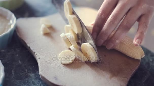 Female hand cuts on pieces banana on wooden board. — Stock Video