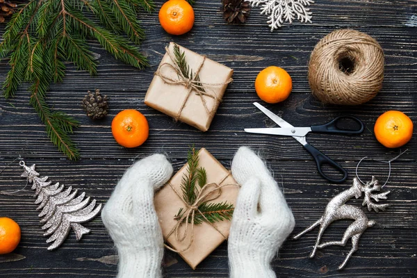 Noel, yeni yıl hediye ya da mevcut kraft kağıt Şerit yukarıda ahşap masa ve beyaz pamuklu dantel yayla sarılı tutan mittens elinde. Üstten Görünüm, düz yatıyordu. — Stok fotoğraf