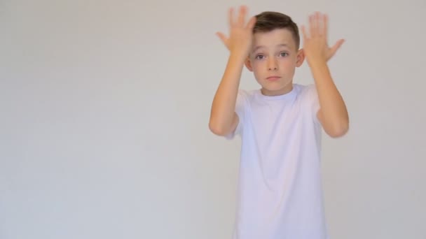 Разочарованный мальчик в белой футболке машет руками на белом фоне . — стоковое видео