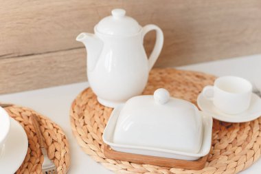 Beyaz seramik sofra takımı, lifli örülmüş yuvarlak masa örtüsü ve beyaz arka planda çatal bıçak seti. İskandinav tarzı.