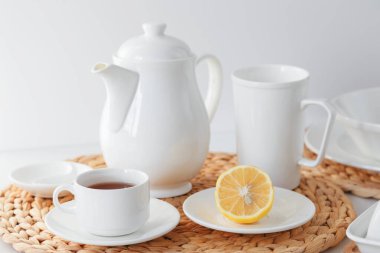 Beyaz seramik sofra takımı, lifli örülmüş yuvarlak masa örtüsü ve beyaz arka planda çatal bıçak seti. İskandinav tarzı