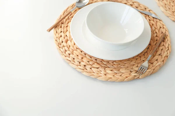 Vajilla de cerámica blanca, mantel redondo trenzado de fibra y cubiertos sobre fondo blanco. Estilo escandinavo . — Foto de Stock