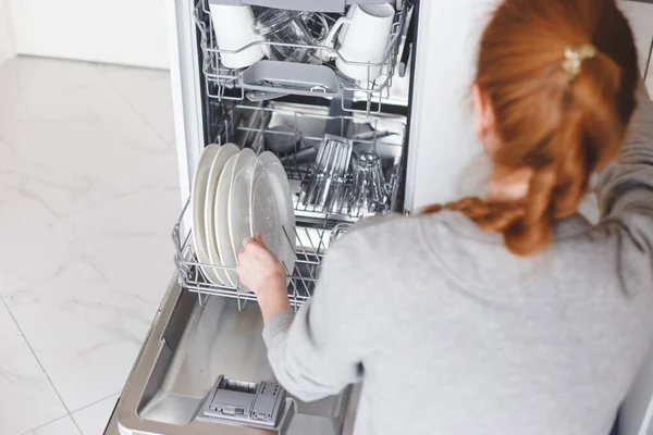 Házimunka: fiatal nő tányérokat tesz a mosogatógépbe — Stock Fotó