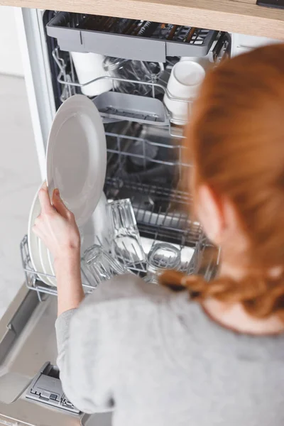 家务活：年轻妇女把碗碟放在洗碗机里 — 图库照片
