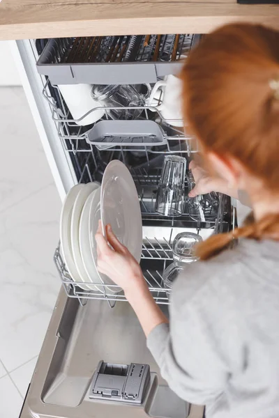 Trabajo doméstico: mujer joven poniendo platos en el lavavajillas — Foto de Stock