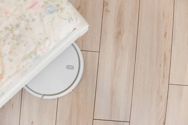 Robot vacuum cleaner vacuuming under the bed. Top view — Stock Photo, Image