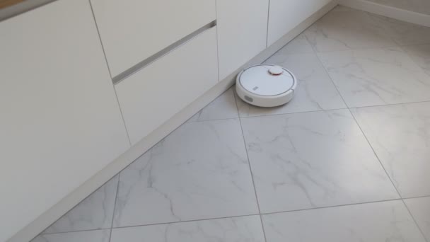 Robot blanco hoover se mueve en el suelo a lo largo de muebles de cocina — Vídeos de Stock