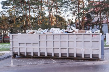 Garbage container full of garbage bags and other wastes with forest in background