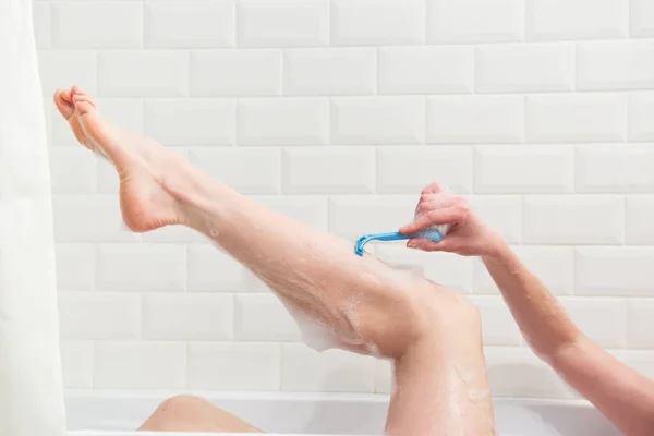 Een vrouw in de badkamer scheert haar benen met een scheermes. Close-up van een hand met een scheermes. — Stockfoto