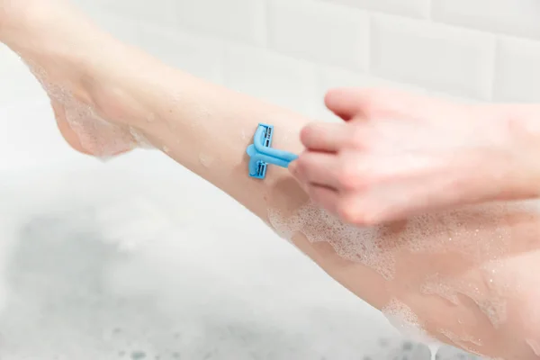 Una donna in bagno si rasa le gambe con un rasoio. Primo piano di una mano con un rasoio . — Foto Stock
