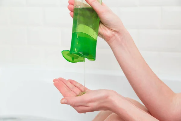 Vrouw giet groene shampoo uit een fles in haar handpalm. Badkamer, haar- en lichaamsverzorging. Milieuvriendelijke cosmetica — Stockfoto