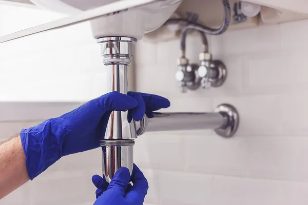 Plumber repairs and maintains chrome siphon under the washbasin. Plumber at work in bathroom, plumbing assemble and install concept — Stock Photo, Image