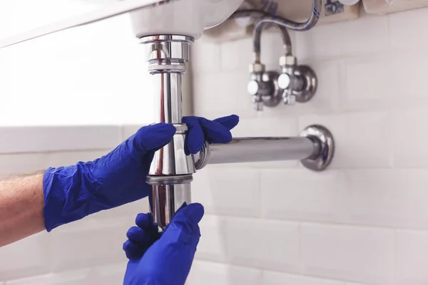 Fontanero repara y mantiene sifón de cromo bajo el lavabo. Fontanero en el trabajo en el baño, fontanería montar e instalar el concepto — Foto de Stock