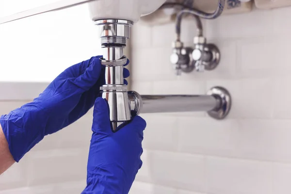 Fontanero repara y mantiene sifón de cromo bajo el lavabo. Fontanero en el trabajo en el baño, fontanería montar e instalar el concepto — Foto de Stock