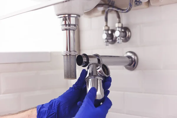 Plumber repairs and maintains chrome siphon under the washbasin. Plumber at work in bathroom, plumbing assemble and install concept — Stock Photo, Image