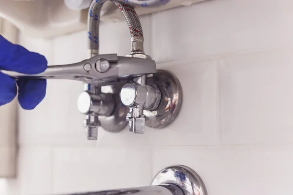 Plumber turns nut on angle valve under wash basin using spreading wrench. — Stock Photo, Image