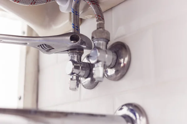 Plumber turns nut on angle valve under wash basin using spreading wrench. — Stock Photo, Image