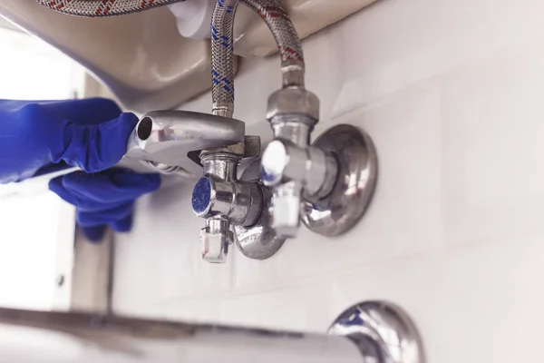 Tesisatçı, lavabonun altındaki açılı vanaya İngiliz anahtarı kullanarak fındık döker..