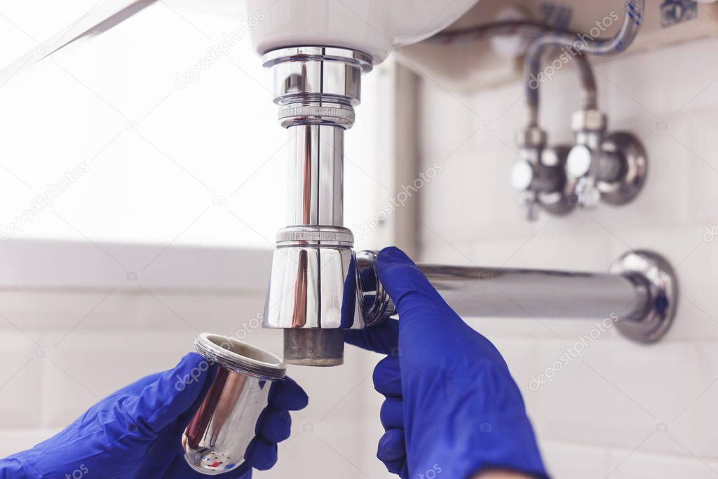 Plumber repairs and maintains chrome siphon under the washbasin. Plumber at work in bathroom, plumbing assemble and install concept