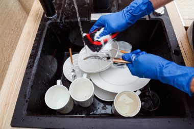 Bulaşıkları yıkamak - Eldiven giymiş bir adam süngerle yıkıyor ve lavaboda akan suyun altında bulaşıkları yıkıyor.