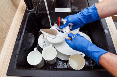 Bulaşıkları yıkamak - Eldiven giymiş bir adam süngerle yıkıyor ve lavaboda akan suyun altında bulaşıkları yıkıyor.