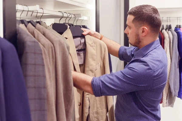 Muž si vybere klasický kabát v obchodě s oblečením, módní butik. — Stock fotografie