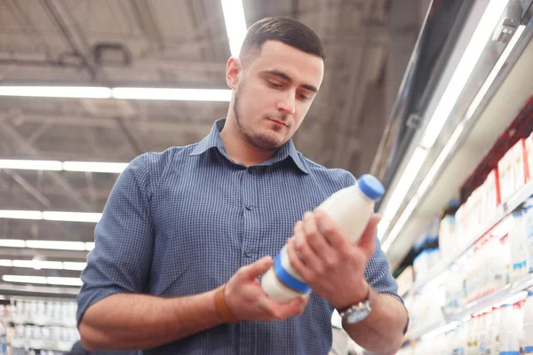 A man read bottle with milk or yogurt in the milk department of the supermarket. A man buys dairy products in the store