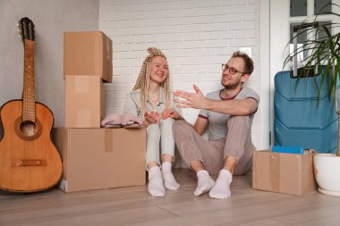 Yeni bir eve taşındıktan sonra genç çift dinleniyor. Eşyaları paketlenmiş bir adam ve kadın.