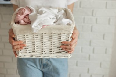 Tuğla duvar arkasında farklı giysilerle hasır sepet tutan bir kadın.