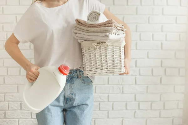 Mujer sosteniendo botella de gel detergente y cesta con montón de ropa diferente antes de la lavandería, sobre fondo de pared de ladrillos — Foto de Stock