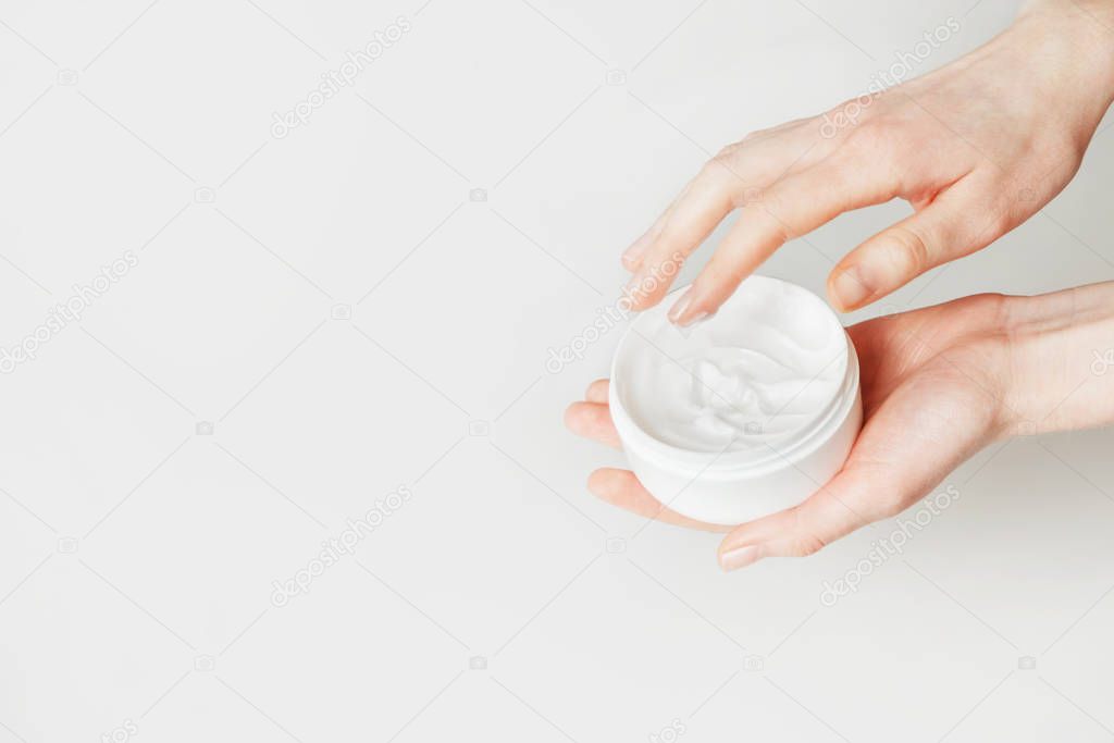 Woman hand touch moisturizer white cream in jar. Isolated on white with copy space