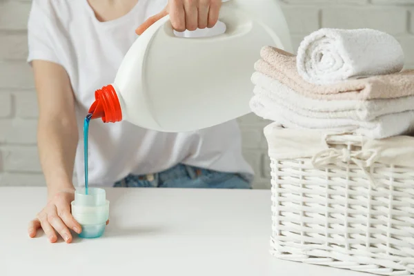 Primer plano de las manos femeninas vertiendo detergente líquido de lavandería en la tapa en la mesa rústica blanca con toallas en la cesta de mimbre — Foto de Stock