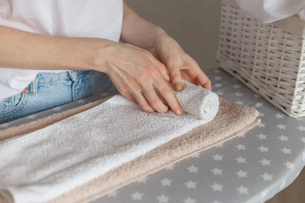 Mujer rodando toallas limpias planchadas de pie en la tabla de planchar. Servicio de lavandería o limpieza concepto de tareas domésticas — Foto de Stock