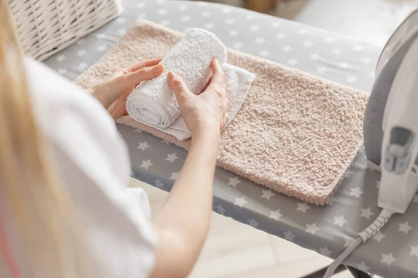 Mujer rodando toallas limpias planchadas de pie en la tabla de planchar. Servicio de lavandería o limpieza concepto de tareas domésticas — Foto de Stock