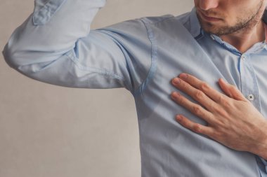 Hiperhidrozlu bir adam mavi gömlekli, gri gömlekli, koltuk altında çok kötü terliyor.