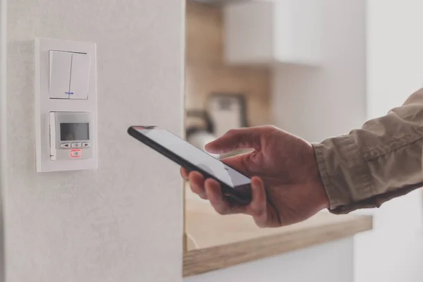 Smartphone aangesloten op vloerverwarming controller in de keuken. Remote home control systeem op een smartphone. — Stockfoto