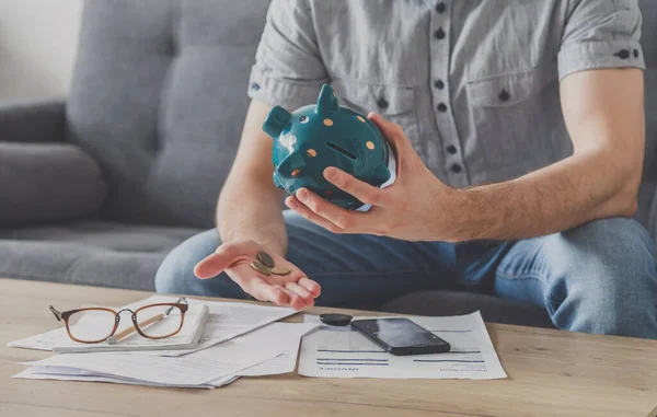 Ödenmemiş faturalarla dolu bir masada oturan adam kumbaradaki son kuruşu da silkeliyor. Son birikimlerini harca. İşsizlik, yoksulluk, iflas kavramı.