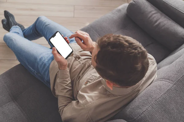 Person holding a phone with blank screen on a couch in the top view of a man wearing a shirt and jeans in the room