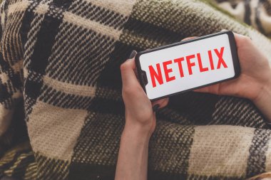 Minsk, Belarus - 01 Mayıs 2020: Netflix servisinin akıllı telefondaki videosunu izleyen kadın