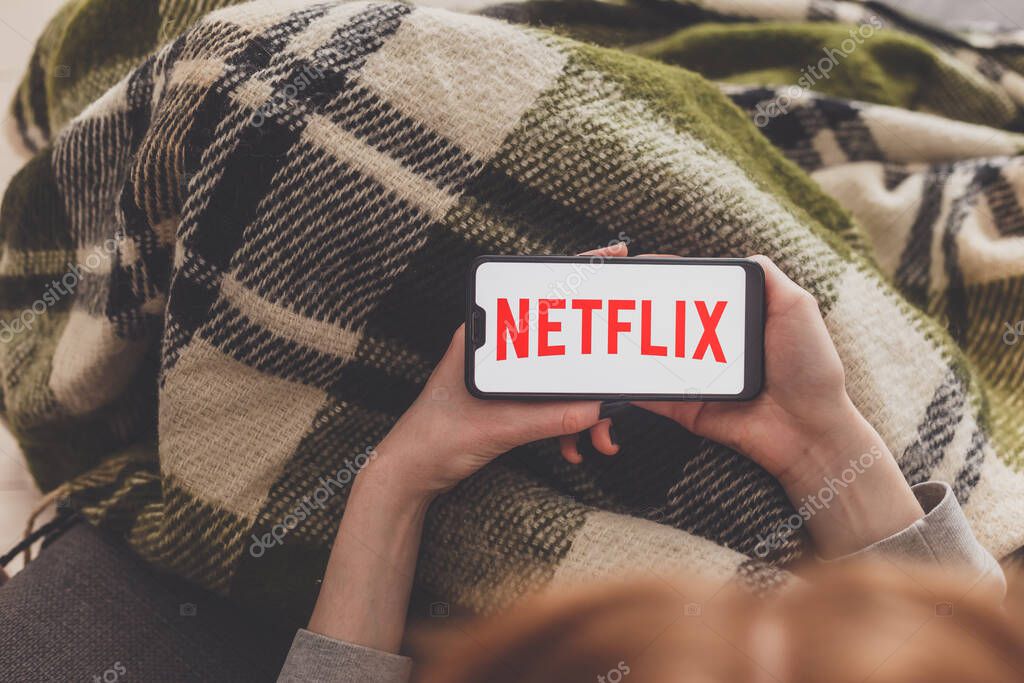 Minsk, Belarus - May 01, 2020: Woman during self isolation watching video by Netflix service on smartphone.