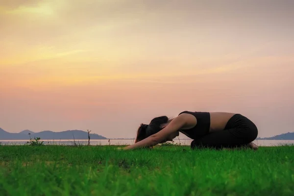 A mulher Yoga é relaxar com belo pôr do sol de fundo no — Fotografia de Stock