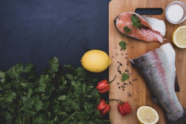 Yeşiller, limon, baharatlar ve somon dilimleri ahşap bir tahtanın üzerinde.