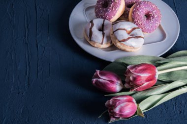 white and pink donuts and red tulips lie on a table 
