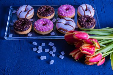 Laleler, küp şekerler ve lezzetli çörekler cam tepside yatıyor. 