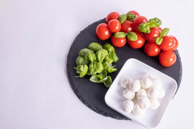 bir fincanda mozzarella, fesleğen ve domatesler beyaz arka planda taş bir fayans üzerinde
