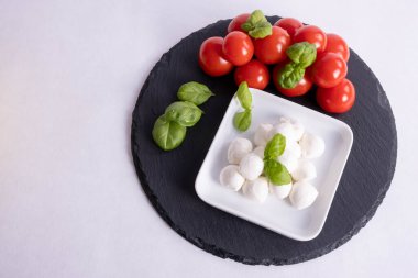 Beyaz bir fincanda mozzarella ve beyaz arkaplanda siyah bir fayans üzerinde domatesler.