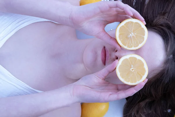 young girl with lemon halves closes her eyes on a white background