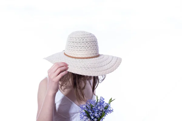 girl under a hat hides her face, in her hands a bouquet of spring flowers on a white background