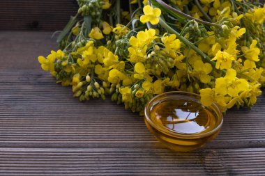 Büyük bir buket çiçek açan kolza tohumu ve yağ sabah ışığında ahşap bir masanın üzerinde.
