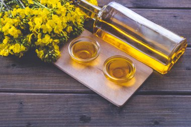 Kolza yağı şişesi ve kolza tohumu dolu bardaklar tahtanın üzerinde duruyor. Tahtadaki genç kolza tohumu çiçeklerinin yanında.